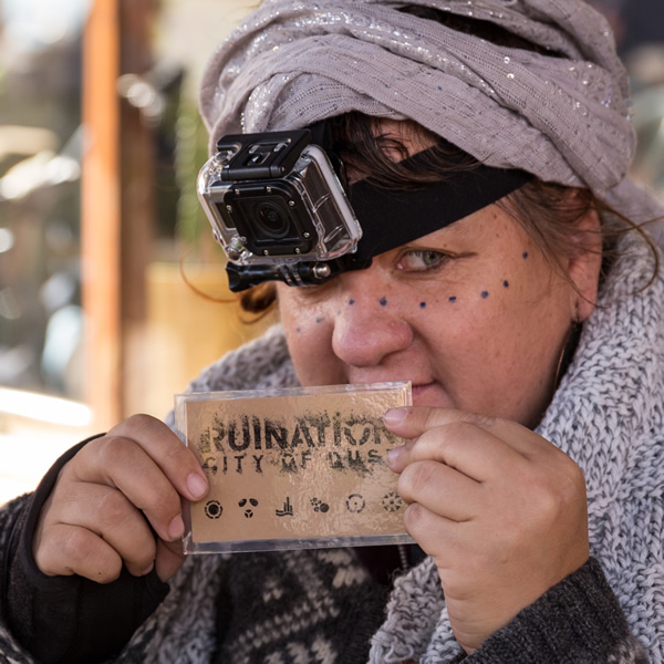 A fortuneteller from the future holds up a card, during Ruination: City of Dust immersive adventure.